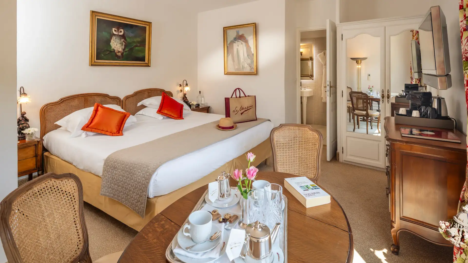 Chambre d'hôtel avec un lit double, une table avec un plateau de petit-déjeuner, des chaises et une porte ouverte sur une salle de bain