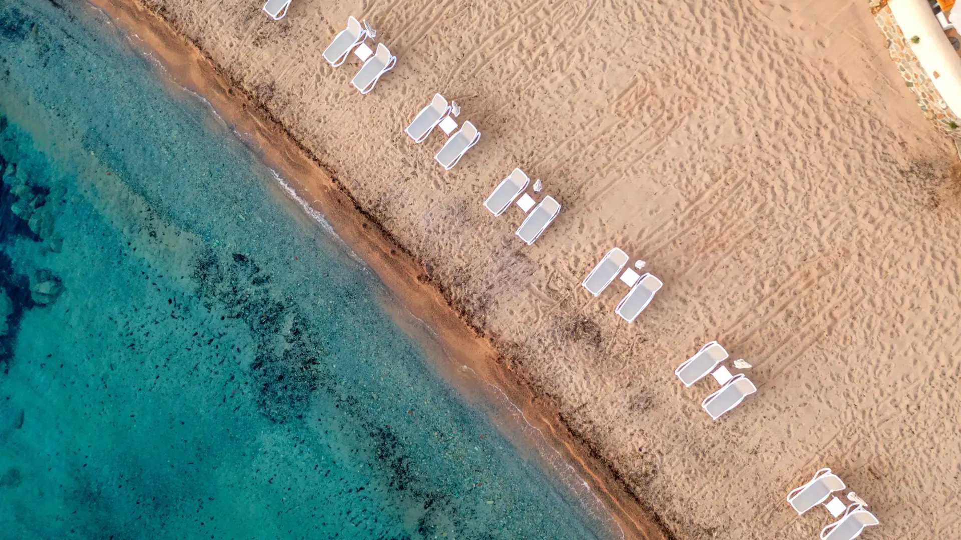 Vue aérienne de transats blancs alignés sur une plage de sable à côté d'une mer turquoise