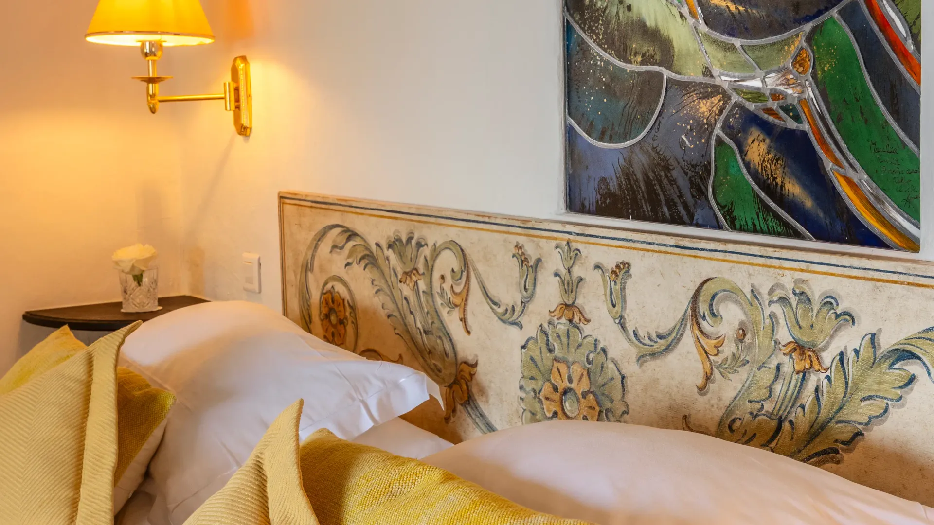 Lit avec une tête de lit décorée, des coussins jaunes et une lampe de chevet allumée, un tableau coloré accroché au mur
