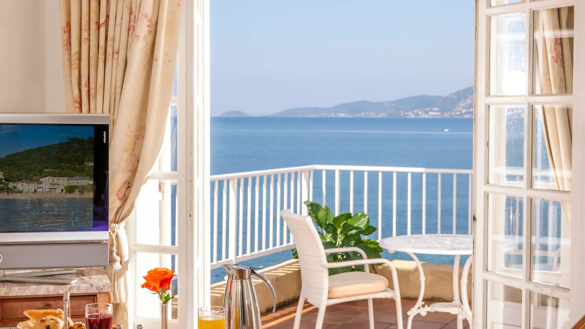Table dressée pour le petit-déjeuner avec vue sur la mer depuis une terrasse avec des chaises blanches
