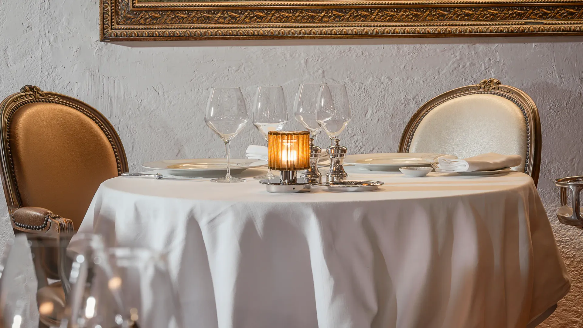 Table dressée avec des verres à vin, des assiettes et une nappe blanche, devant un tableau encadré au mur