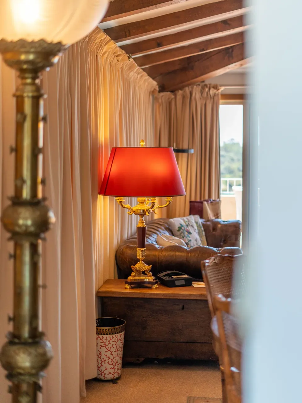 Une lampe à abat-jour rouge est posée sur une table en bois à côté d'un canapé dans un salon aux poutres apparentes